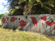 red flowers painted on the side of a wooden fence in front of trees and grass