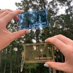 two hands holding up a cell phone in front of trees