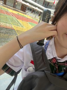 a girl is holding her hand up to her ear and looking at the camera with a tennis court in the background