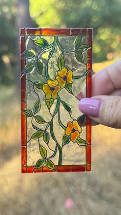 a hand holding up a small stained glass block with yellow flowers on it's side