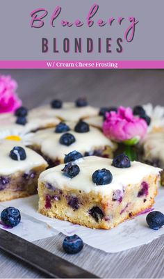 blueberry blondies with cream cheese frosting on a cutting board next to flowers