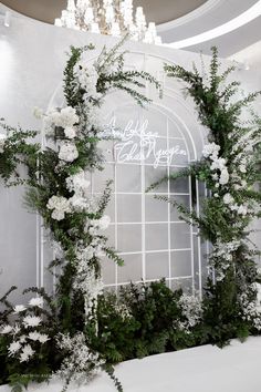 an arch decorated with flowers and greenery in front of a window