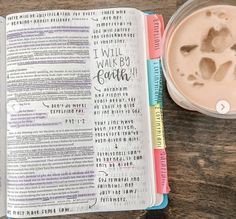 an open bible next to a cup of coffee on top of a wooden table with writing in it