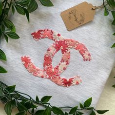 a white towel with pink and red flowers on it next to some green leaves in front of a tag