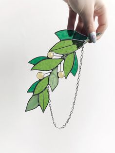 a hand holding a piece of paper with green leaves on it and beads attached to the chain