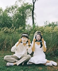 two children sitting on the ground holding up their cell phones in front of their faces