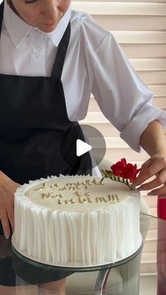 a woman in an apron is cutting into a cake with white frosting and red flowers