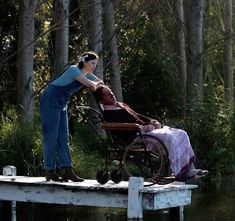 a woman pushing a baby in a stroller on a dock next to the water