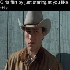 a man wearing a cowboy hat standing in front of a wooden wall with the caption girls first by just starting at you like this