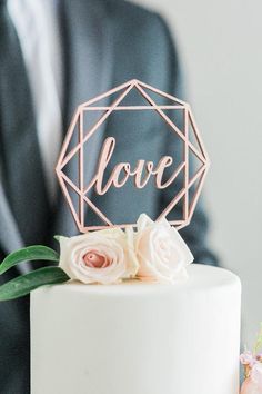 a close up of a white cake with pink flowers on top and a man in a suit behind it