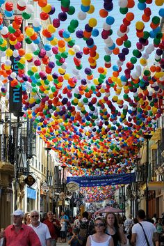 people are walking down the street with many colorful balloons hanging from the ceiling above them