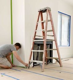 a man that is kneeling down in front of a fire place with a ladder on the floor