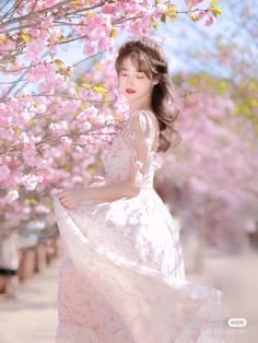 a woman in a white dress standing under a tree with pink flowers