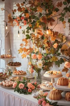 a table topped with lots of desserts and flowers next to a wall covered in leaves