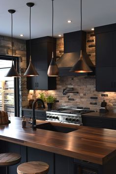 a kitchen with black cabinets and wooden counter tops, two pendant lights over the island