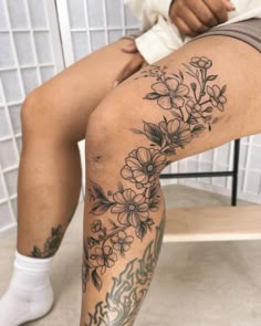 a person sitting on a chair with flowers tattooed on their legs