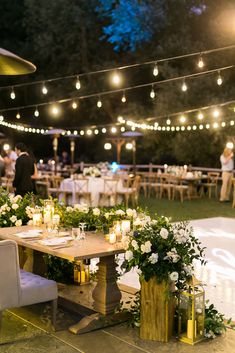 an outdoor event with tables, chairs and flowers on the table are lit by string lights