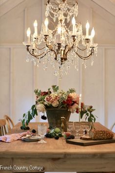 a chandelier hanging from the ceiling over a table with flowers and wine glasses