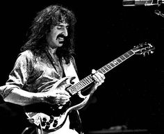 a black and white photo of a man playing an electric guitar with his mouth open