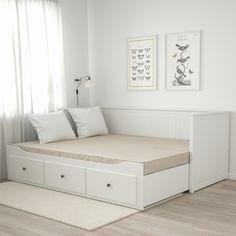 a white bed with drawers underneath it in a room next to a window and curtains