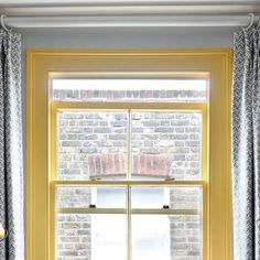 a window with yellow curtains and a brick wall in the background is an old fashioned bathtub