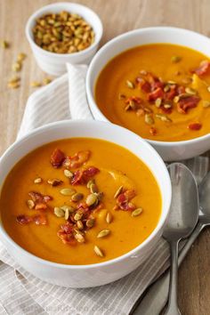 two white bowls filled with soup on top of a wooden table next to spoons