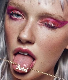 a woman with pink lipstick and gold chains sticking out her tongue