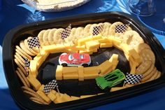 a tray with crackers, cheese and cars on it sitting on a blue table cloth