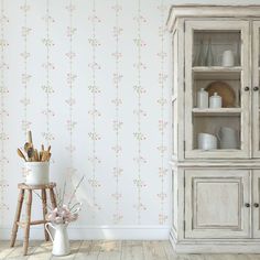 a white china cabinet sitting in front of a wallpapered wall with pink flowers