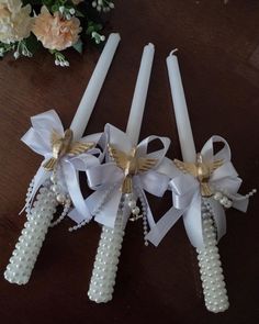 three white candles with bows and pearls on them sitting on a table next to flowers