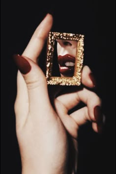 a woman's hands holding up a golden square frame with a red lipstick painted on it