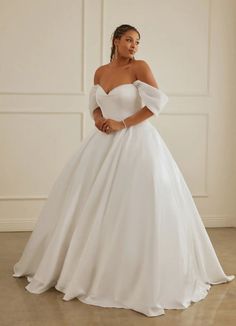 a woman in a white wedding dress standing on the floor with her hand on her hip