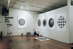 a man sitting on the floor in front of some art work hanging on the wall