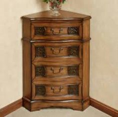 an ornate wooden chest of drawers in a corner with a vase on the top shelf