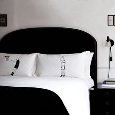 a bed with white sheets and black headboard in a bedroom next to pictures on the wall