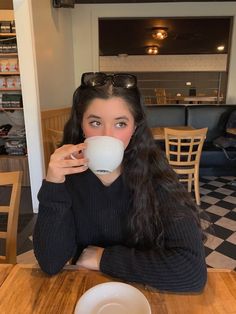 a woman sitting at a table drinking from a cup