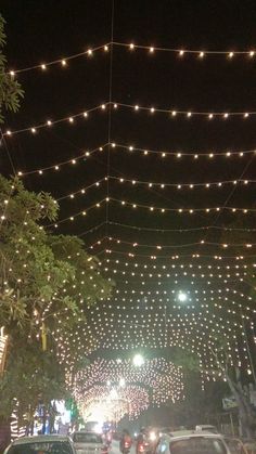 cars are parked on the street under string lights