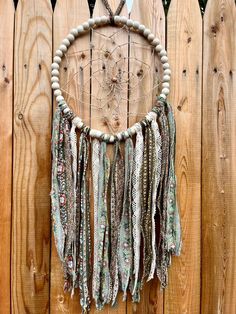 a wooden wall hanging with beads and tassels on it's sides next to a fence