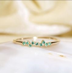 three stone ring in gold with green stones on the side and white cloth behind it