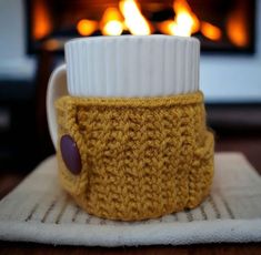 a knitted coffee cup cozying in front of a fire place with the lid off