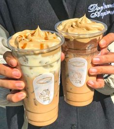 two people holding up cups with different types of drinks in them, one has whipped cream and the other has caramel