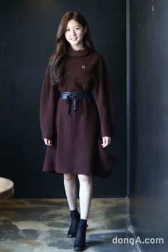 a woman in a brown sweater dress and black booties is posing for the camera