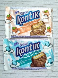 two packets of kontik are sitting on a white brick wall and one is filled with milk