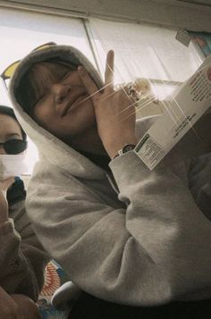 a woman wearing a hoodie is reading a book while sitting on a bus with other people in the background