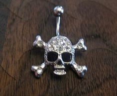 a silver skull and crossbones belly ring on a wooden table with black eyes