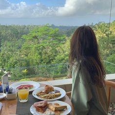 a woman sitting at a table with plates of food on it looking out over the jungle