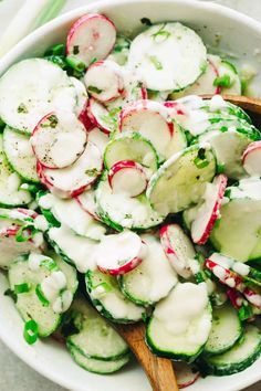 cucumber and radish salad in a white bowl with wooden spoons