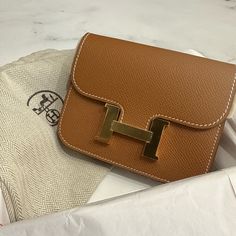 Herms Gold Epsom Constance Slim Gold Hardware, 2022 The Interior Is Lined With Tonal Swift Leather Includes Dust Bag And Box Sizes: Height: 3.94 Inches / 10 Cm Width: 4.92 Inches / 12.5 Cm Depth: 0.79 Inches / 2 Cm Comes With Box And Dust Bag Luxury Tan Wallet As Gift, Luxury Tan Wallets For Gift, Hermes Constance Slim, Mini Constance Hermes, Constance Bag Hermes, Black Constance Hermes, Luxury Wallets With Gold-tone Hardware As Gift, Hermes Constance Wallet To Go, Hermes Constance Bag