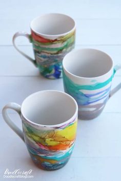 three coffee mugs with colorful designs on them sitting on a white counter top next to each other