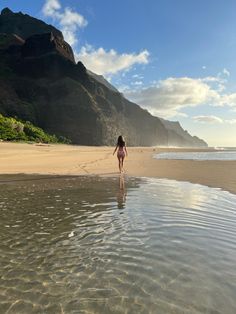 a woman walking on the beach in front of some mountains and water with her back to the camera